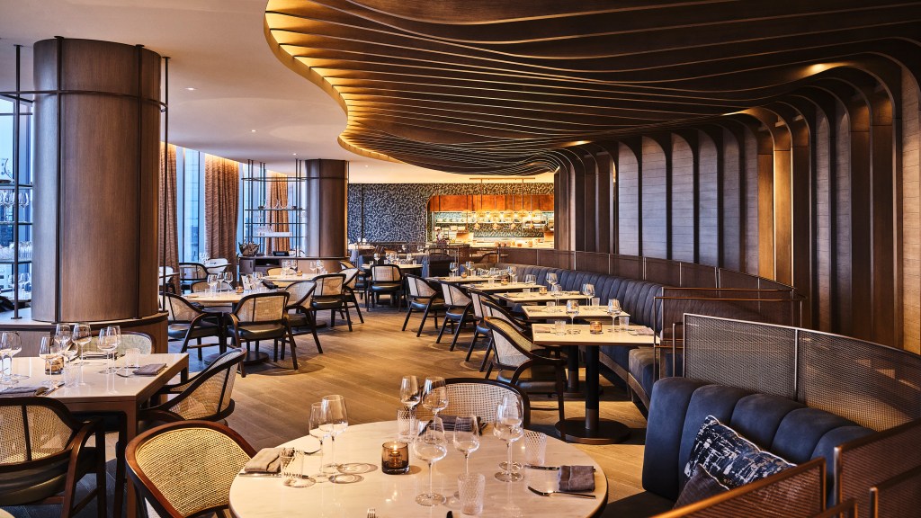 A pulled out view of the Bellpine dining room with multiple seating options, carved wood ceiling panels and the open kitchen at the far end of the room.