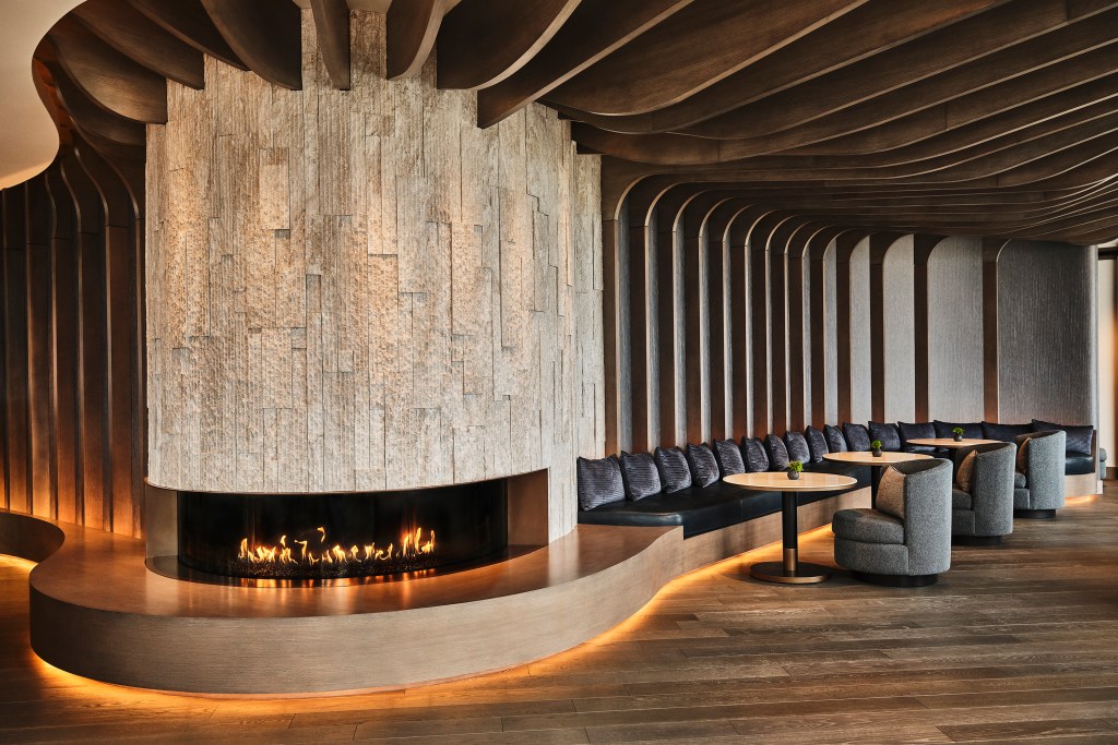 The lounge area of Bellpine with curved stone walls, a fireplace and carved ceiling panels that resemble a ship or animal ribs.