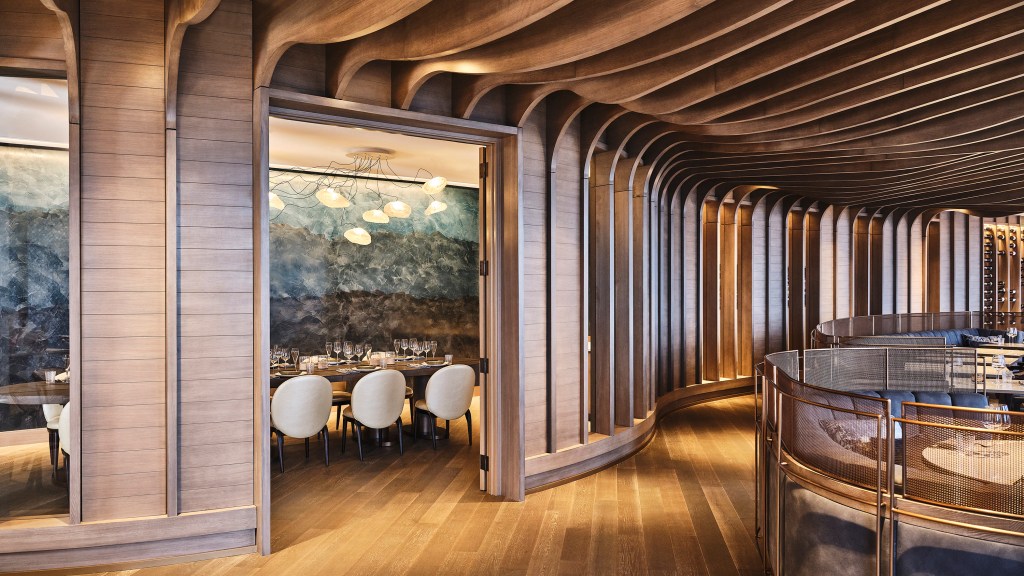 A view into the private dining room at Bellpine with carved wood wall and ceiling panels, a long dining table with white chairs, and a light fixture that resembles a group of jellyfish.