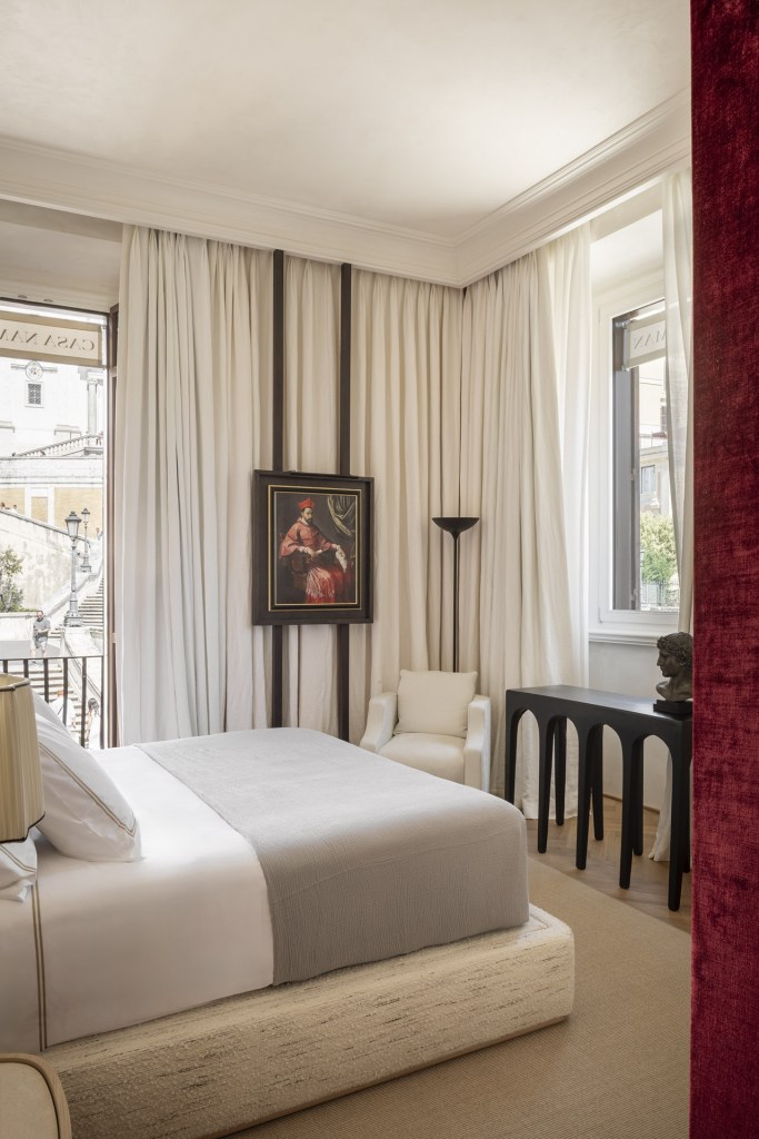 A bedroom at Casa Naman with a view of the Spanish Steps peeking from behind a long cream curtain with a historic painting hanging in front.