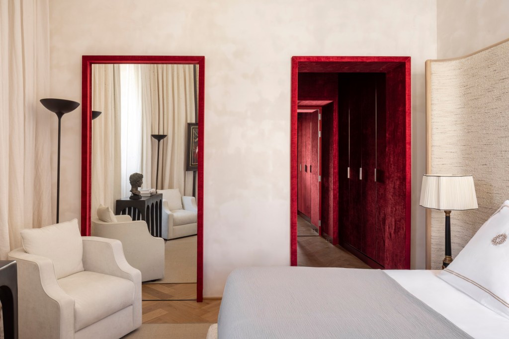 A bedroom at Casa Naman with a red-framed mirror, a red galley closet, and long cream curtains.