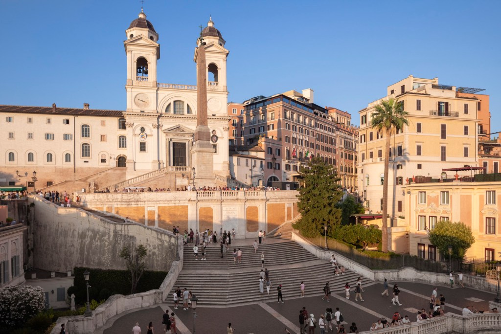 The Spanish Steps in Rome with people walking at sunset.