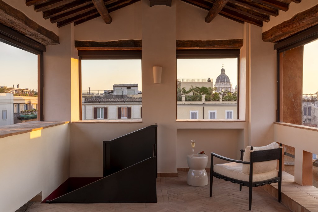 A private rooftop space at Casa Naman with a black metal stairwell, a chair, and two windows overlooking the tops of nearby Roman buildings.