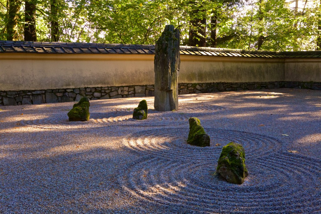 A stone meditation garden with carefully raked stones in a spiral pattern wrapping around large stones.