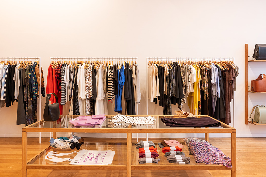 A rack of colorful clothing at Frances May and a glass and wood table with other soft goods artfully arranged.