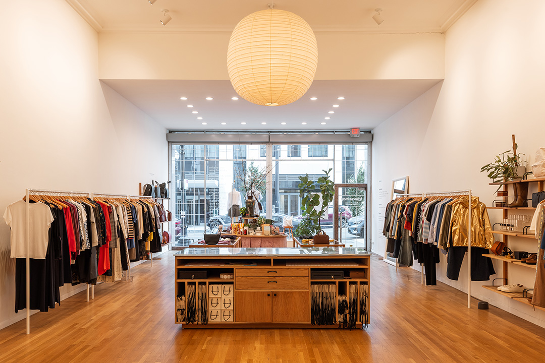 A view of Frances May shot from the back of the store, looking out at the cash register, racks of clothing along the wall, a large paper globe light and the large front doors of the space.