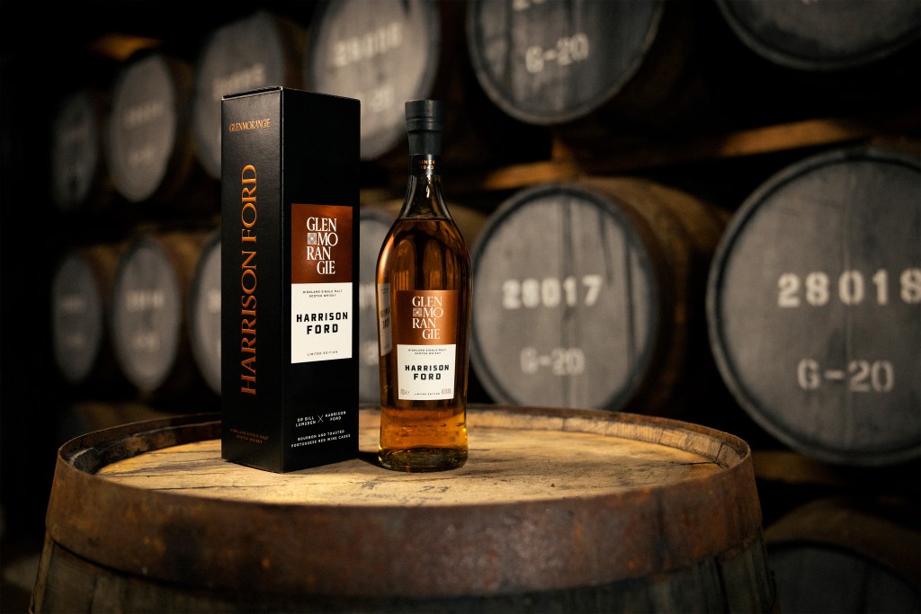 A bottle and accompanying box of Harrison Ford's limited edition collaboration of Glenmorangie single malt scotch with barrels in the background with moody lighting.