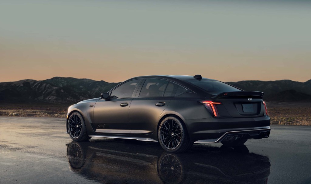 A matte black Cardillac CT5 Blackwing shot from the side on a dark road and sunset in the background.