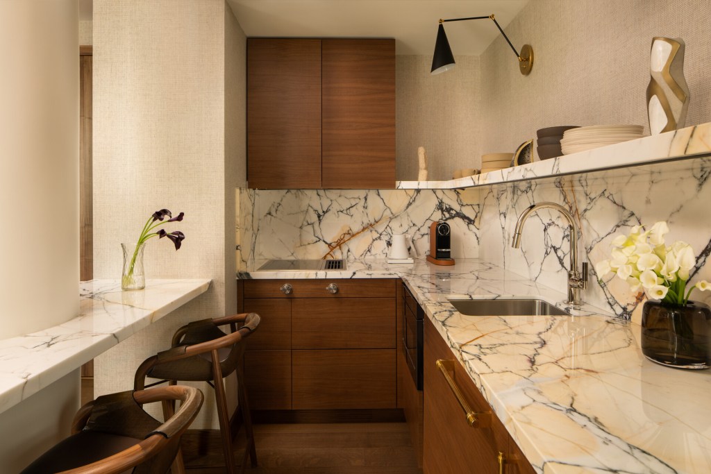 A kitchen at a suite in Four Seasons New York Downtown with a marble counter and backsplash, wood cabinets and a black light over the sink.
