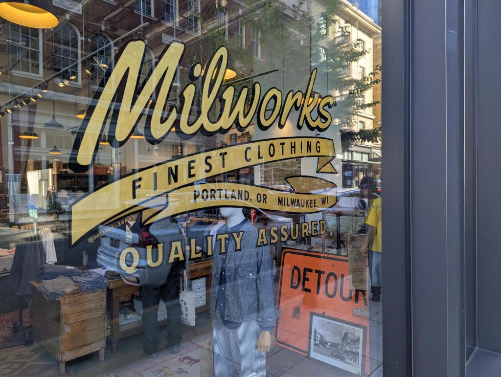 A detail of a hand-painted window sign that says "Milworks--FINEST CLOTHING--Portland, OR Milwaukee, WI.