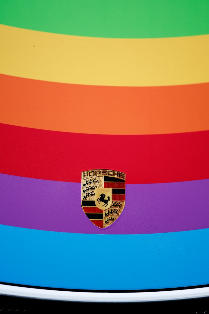 A detail of a Porsche nameplate on a racecar with rainbow stripes on the car.
