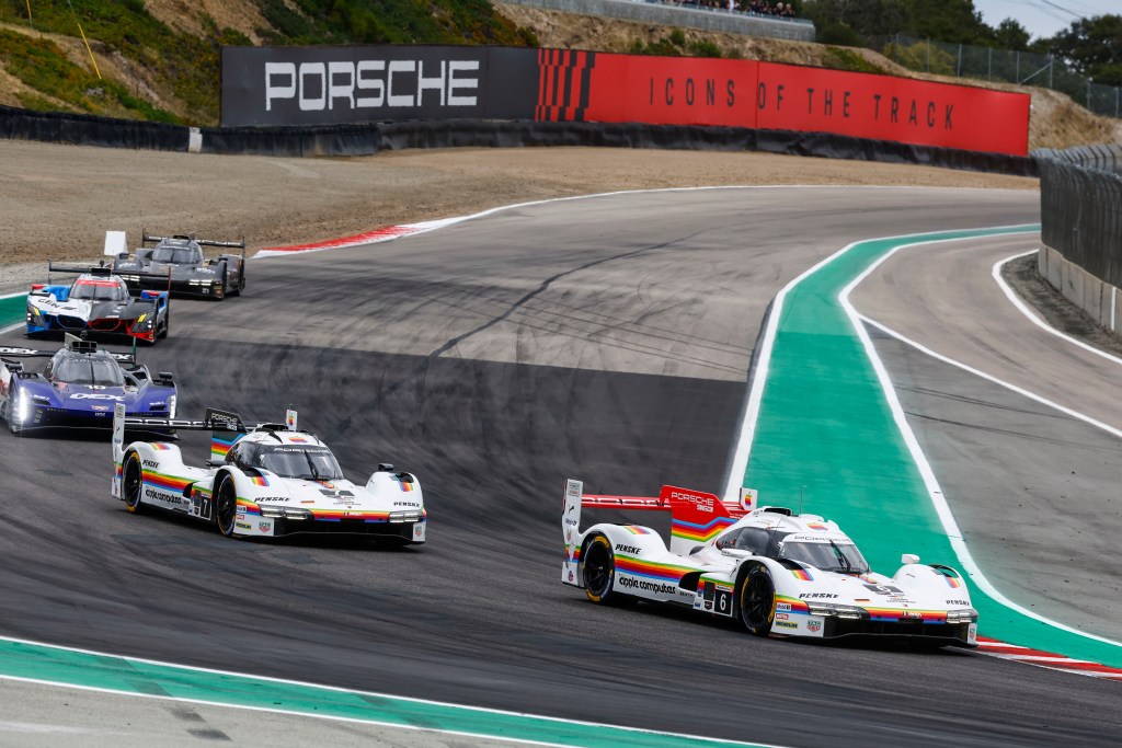 Two Porsche racecars with vintage Apple Computer graphics racing against three other cars at the IMSA Monterey SportsCar Championship 2026 with a large Porsche sign in the background.