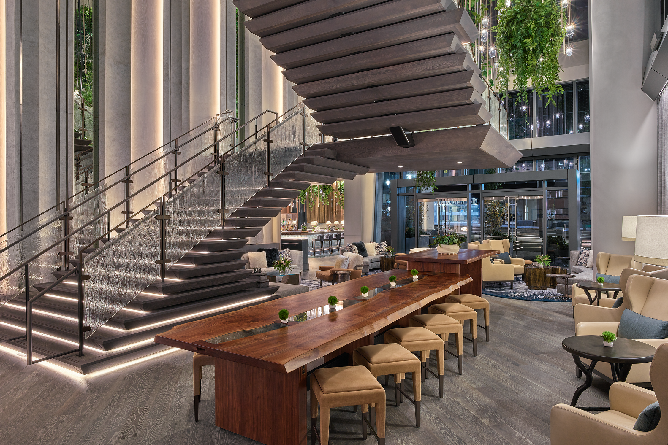 A long wood communal table with large gray and glass stairs behind it.