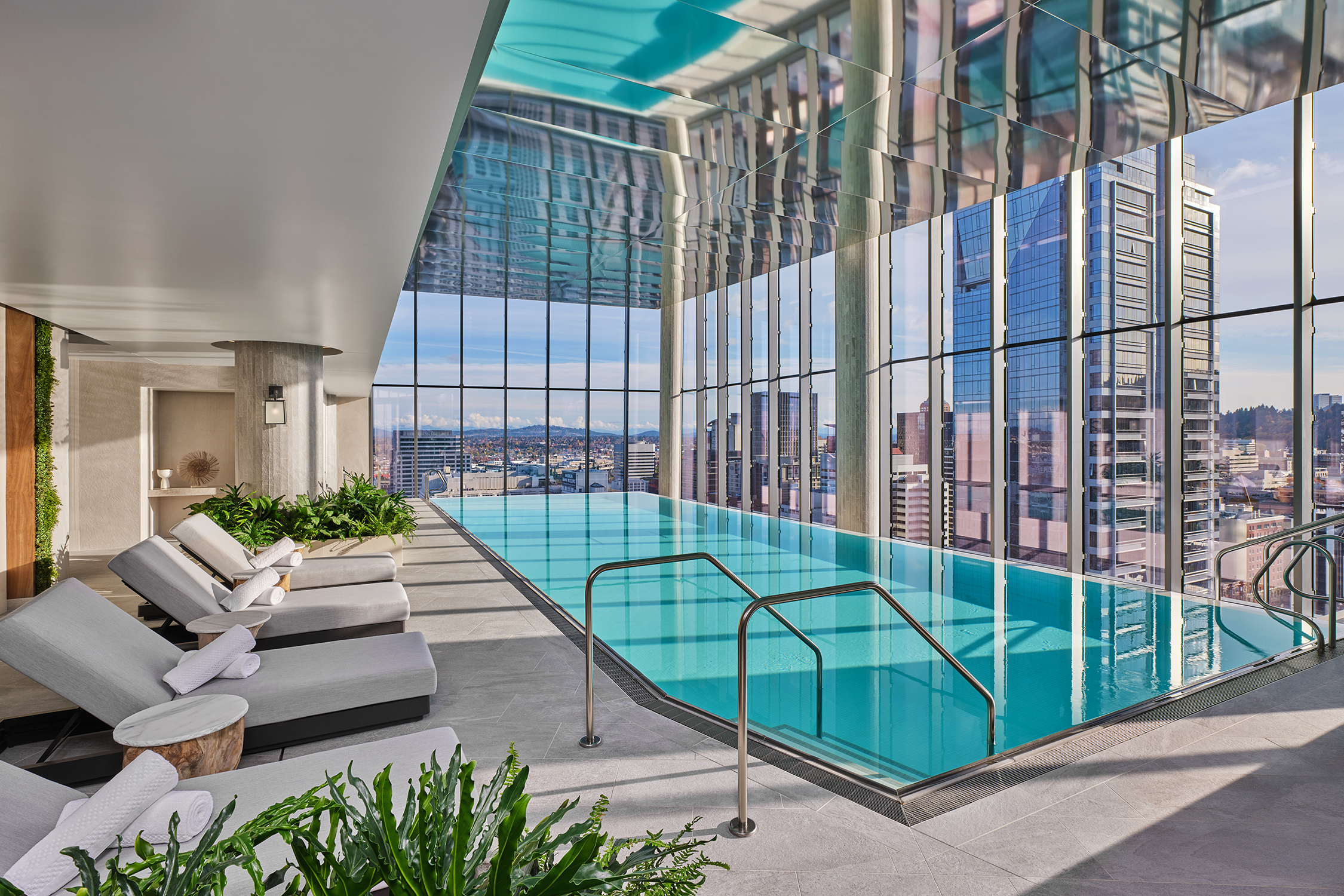 An indoor infinity pool with views of sky and buildings out the tall glass windows.