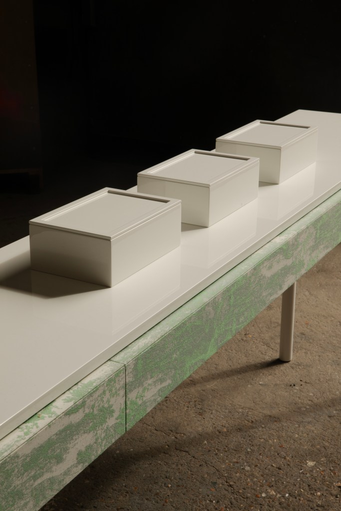 A detail of a white and green modern table with three minimal boxes on top of it, running diagonally in the frame.