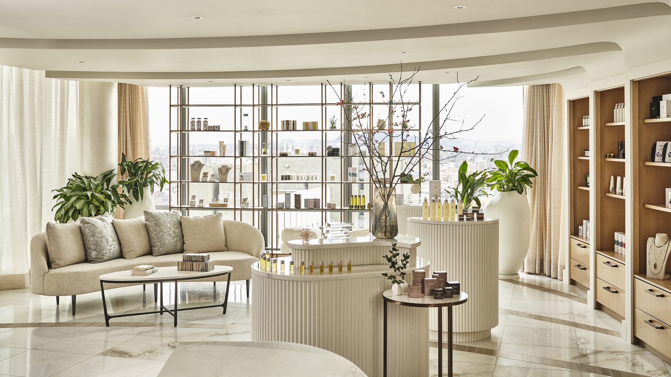 The retail area at The Ritz-Carlton Spa, Portland with white furniture, plants and sun streaming in through the windows, illuminating a collection of beauty products.