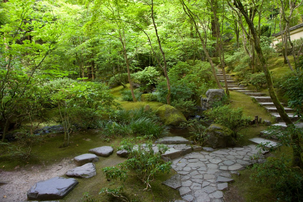 The intersection of two pavement styles in the Portland Japanese Garden, surrounded by green plants and trees.