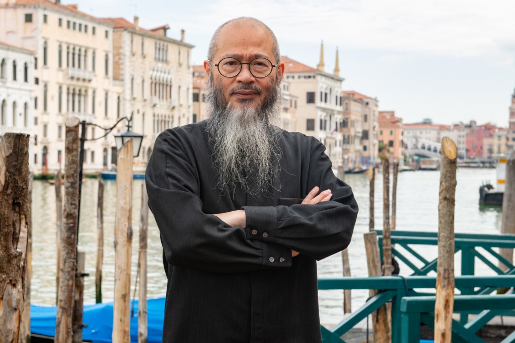 Wallace Chan wearing a black shirt with crossed arms, standing on a dock in front of a Venice canal.
