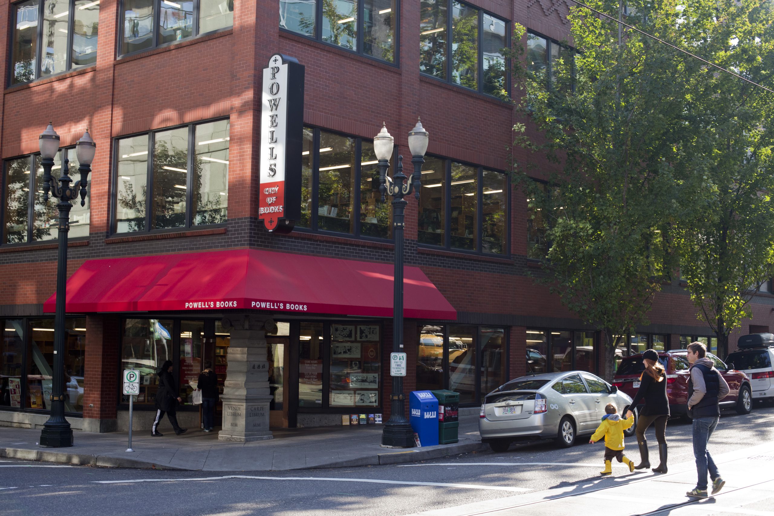 An exterior corner view of Powell's Books in Portland, with a red awning above the store entrance and a large vertical sign hanging from the corner of the brick building.