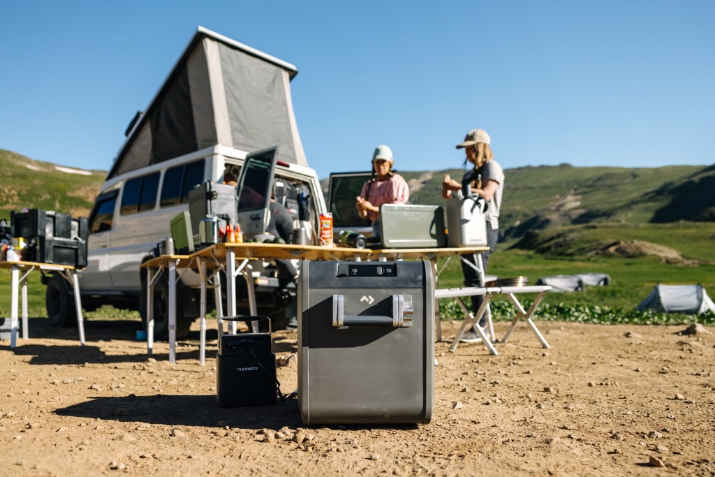 A group of people prepping a meal in front of a car with a pop-up tent, with coolers and other accessories on the table.