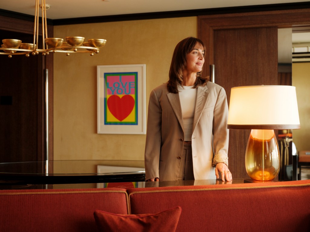 45 Park Lane art curator Lily Ackerman standing behind an orange sofa, looking off to the right, with a lamp and a framed piece of art behind her.