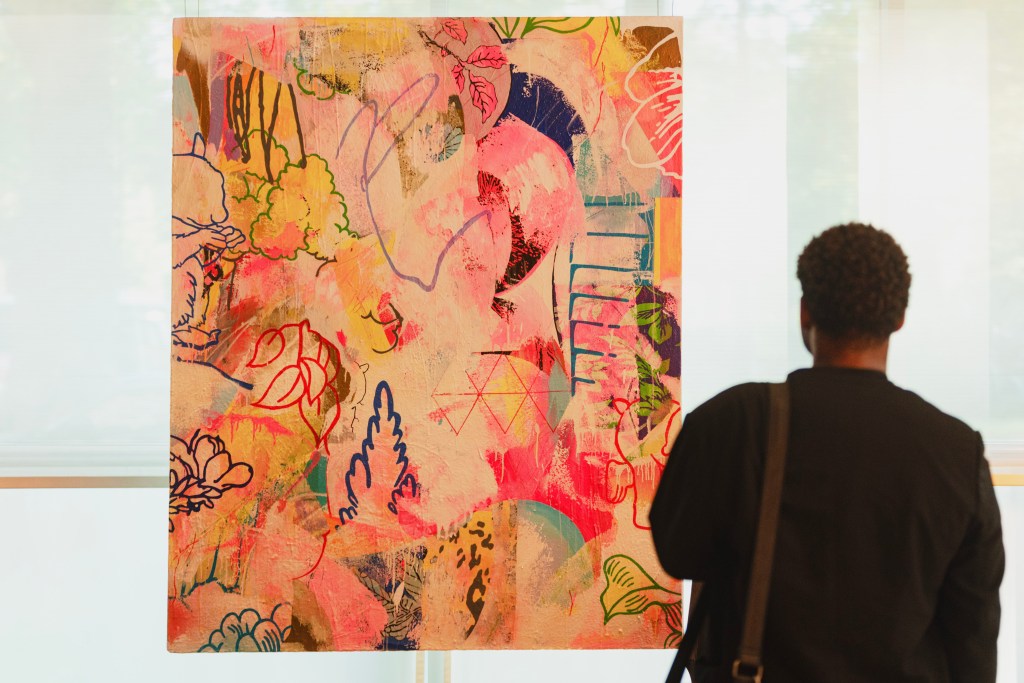 A view of the back of a person as they look at a bright abstract painting by Dan Baldwin.