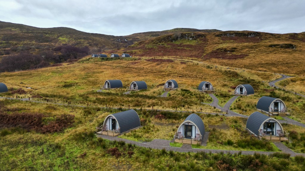 Several small huts with front porches scattered across a hillside on a sunny day.