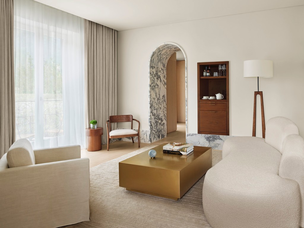 A guest room at Lake Como EDITION with an arched doorway, marble textures and minimal furniture.