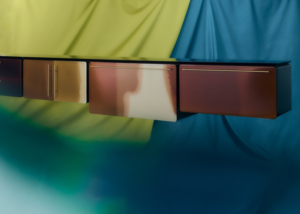 A brown lacquered piece of furniture from Draga & Aurel on a colorful fabric background.