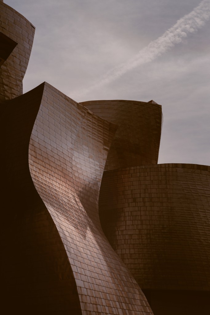 An exterior view of the Guggenheim Museum Bilbao with a moody sky.
