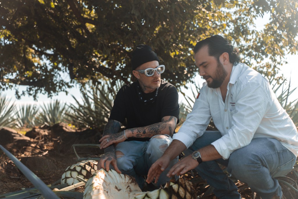Michael Voltaggio and Bruno Barba crouching by a harvested agave plant under a tree.