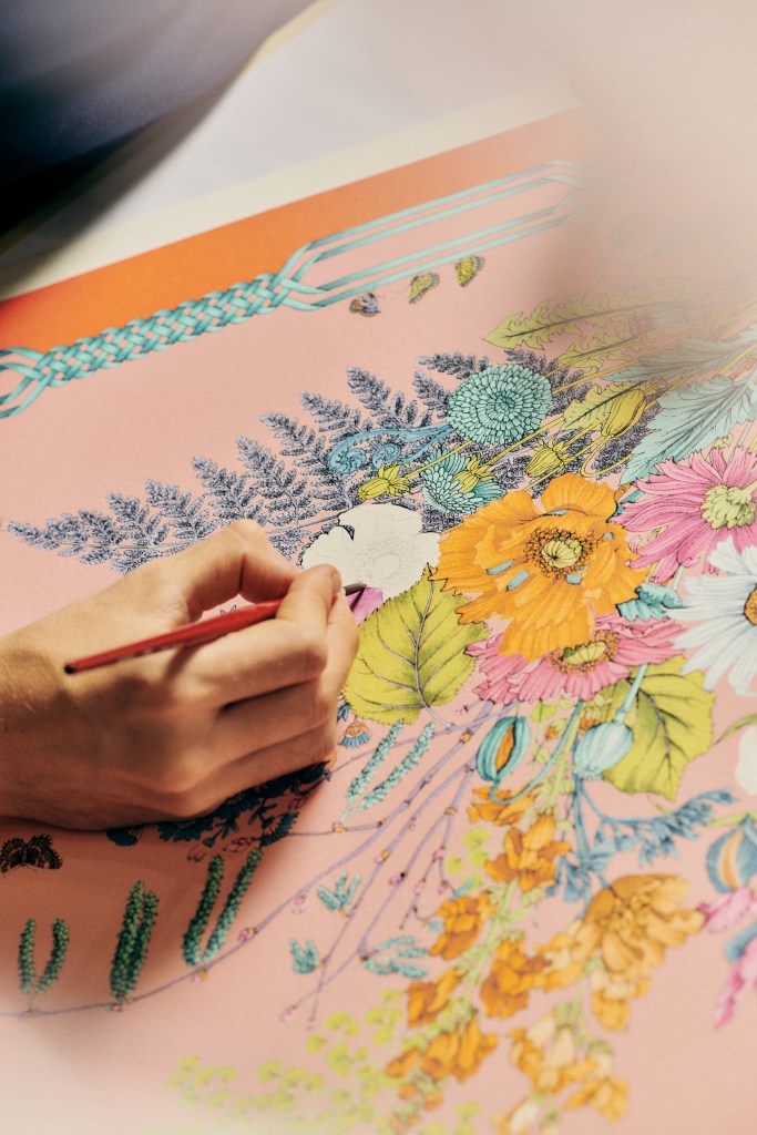 A hand holding a paintbrush and painting a floral design on a piece of paper.