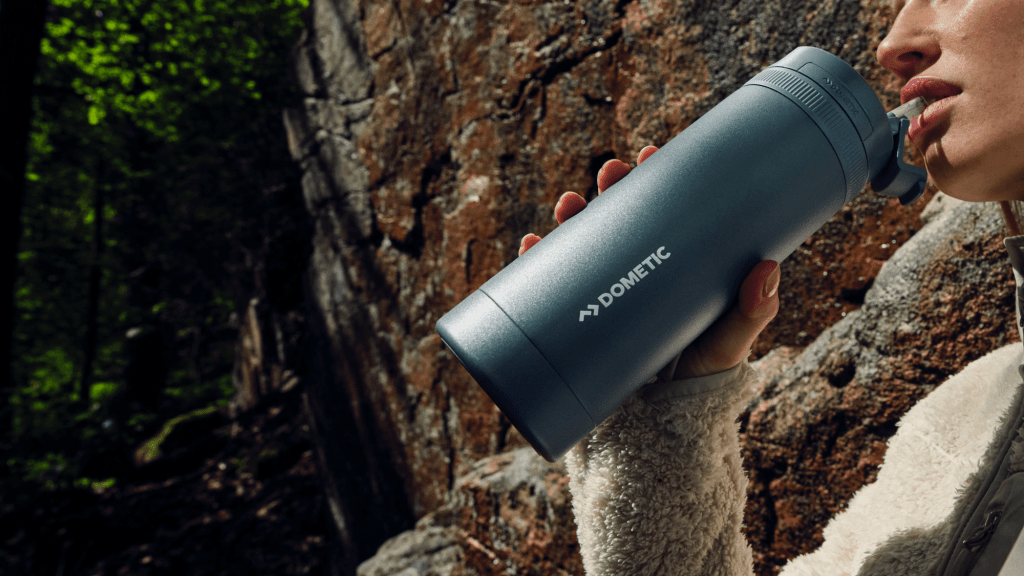 A person holds a large Dometic water bottle with the straw-style lid held up to their lips.