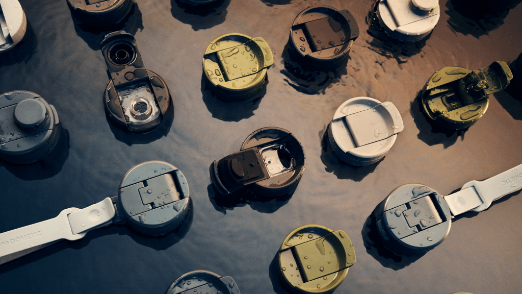 An overhead shot of different colors and styles of Dometic water bottle lids, shot on a gray, water-like surface.