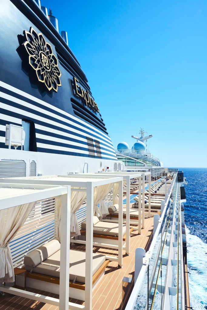 An exterior view of Explora I with a navy blue striped hull, teak decking and private cabanas overlooking the ocean.