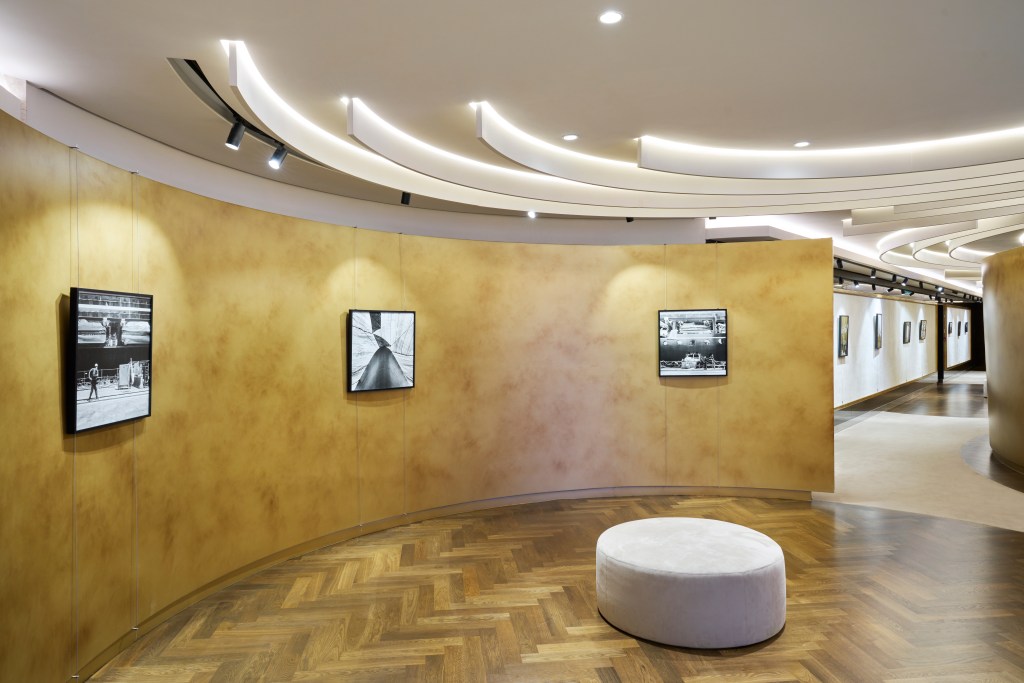 An art gallery room with curved walls displayed framed art and small, circular gray stools for sitting.