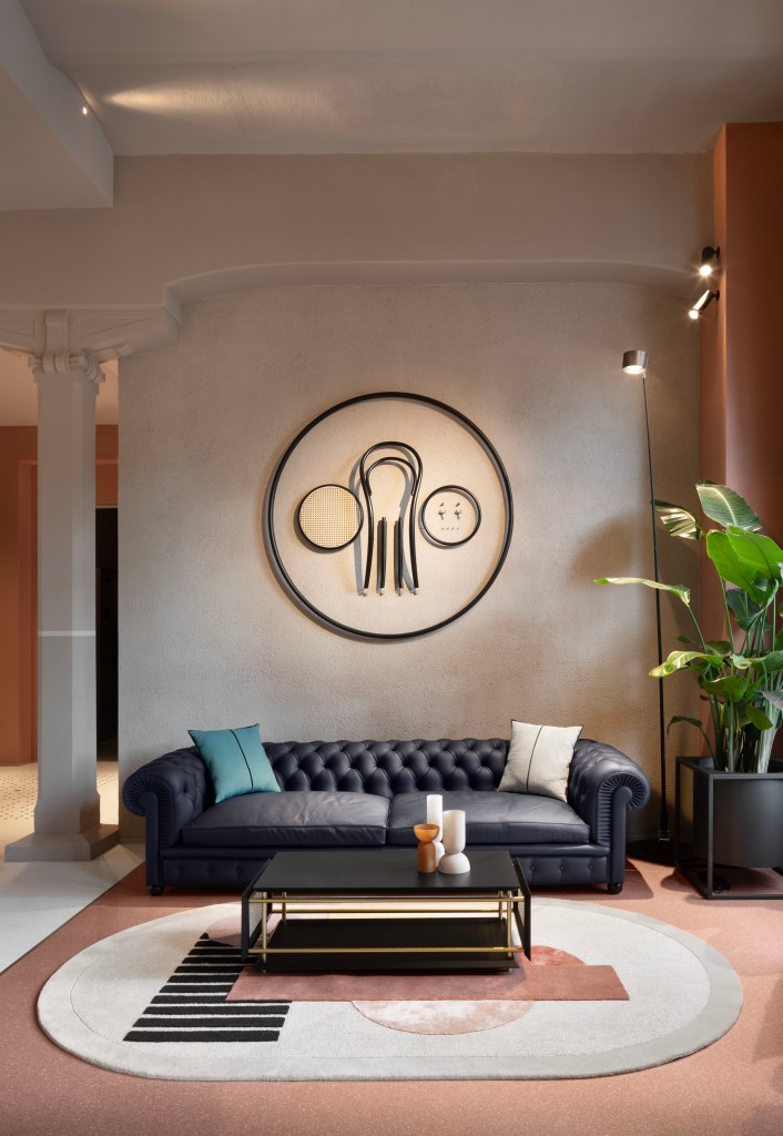 A simple tan room with a low, leather sofa, a round neutral rug and a disassembled Thonet chair hanging on the wall.