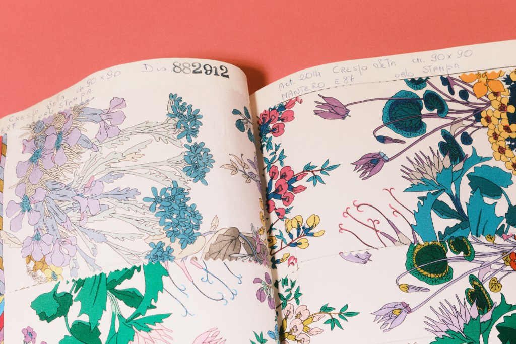 A detail of a textile design archive book shot on a coral background.