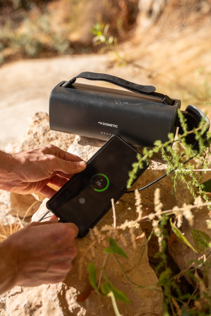 A Dometic PLB15 portable battery charging a phone with a hand holding it.
