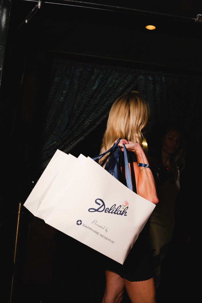 A woman with long blonde hair holding a large white bag that says "Delilah" on the side.
