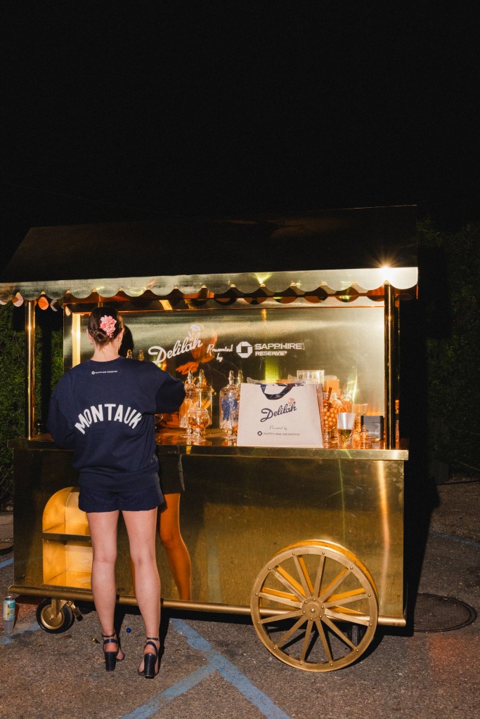 A woman wearing a MONTAUK hoodie in front of a gold bar cart.