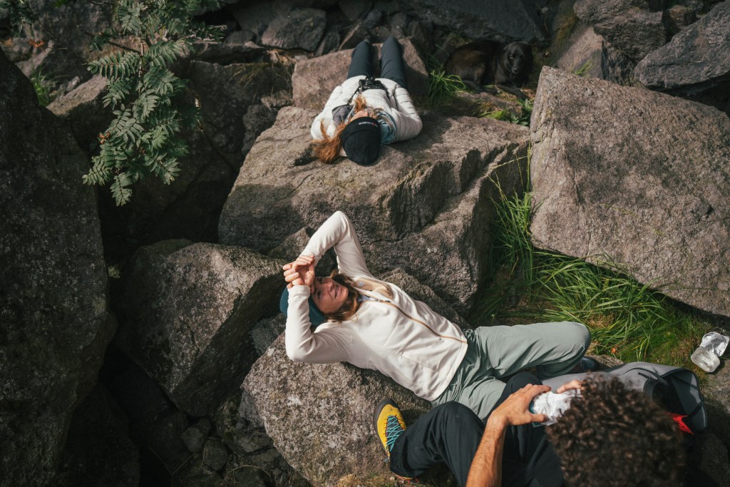 Three rock climbers rest on large boulders, wearing Black Diamond Rift Fleece jackets.