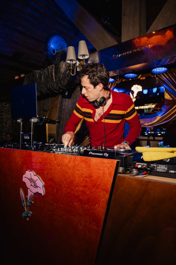 Mark Ronson wearing a red striped shirt DJing on the stage at Delilah.