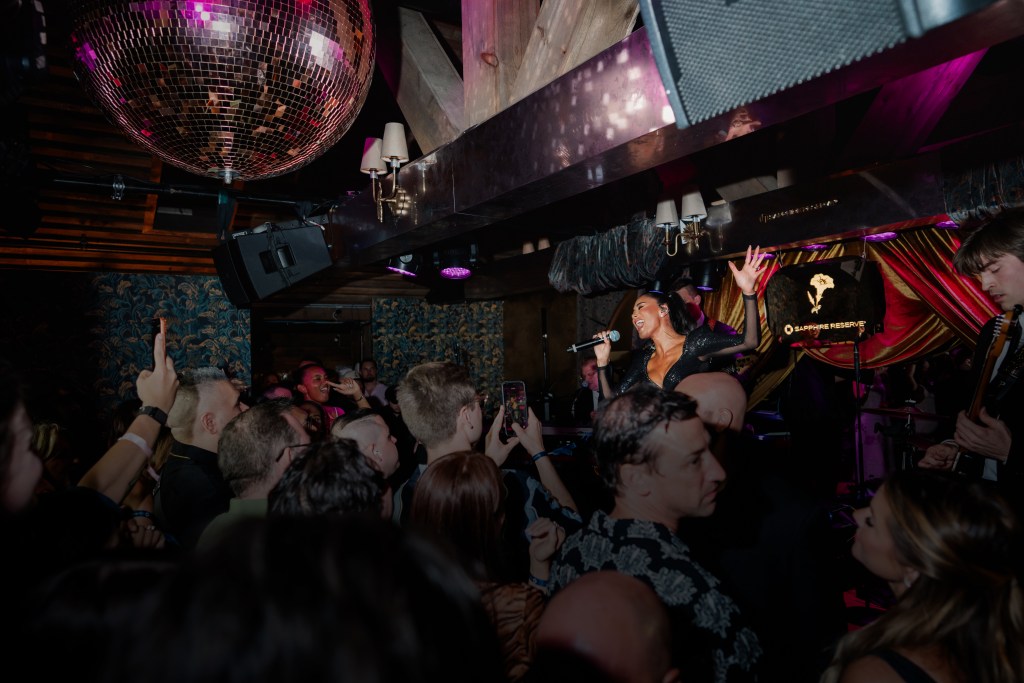 Nicole Scherzinger sings onstage with a crowd of people dancing below.