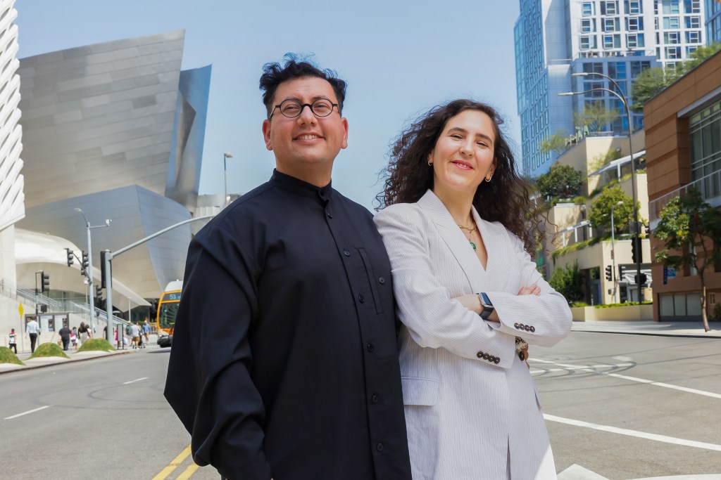 Refik Anadol and Efsun Erkilıç standing on the street in downtown LA in front of their museum at The Grand LA.