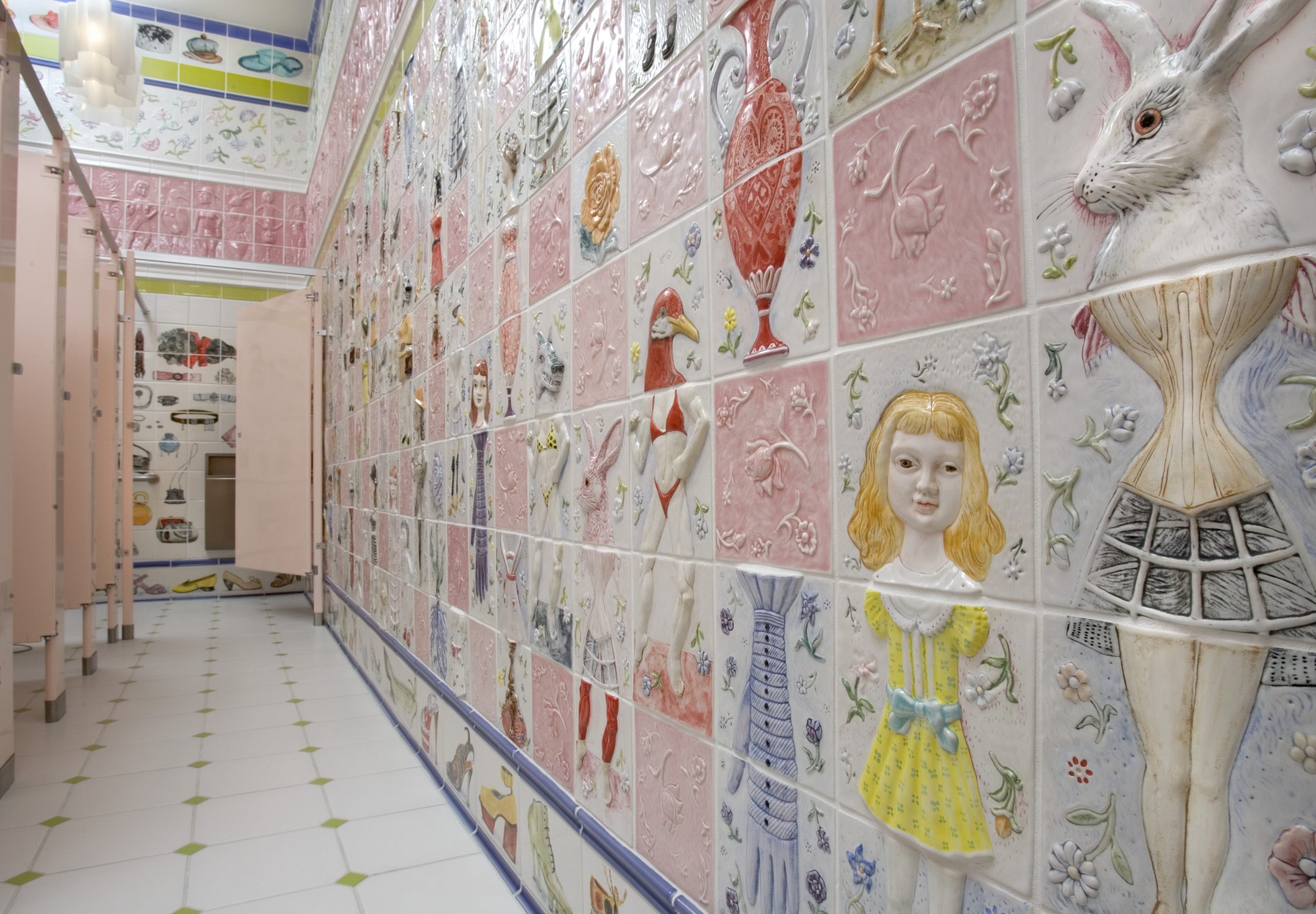 A hallway in a washroom at John Michael Kohler Arts Center designed by Cynthia Consentino with pale pink stall doors and tiles with various women's bodies and objects sculpted in vitreous china and colored glazes.