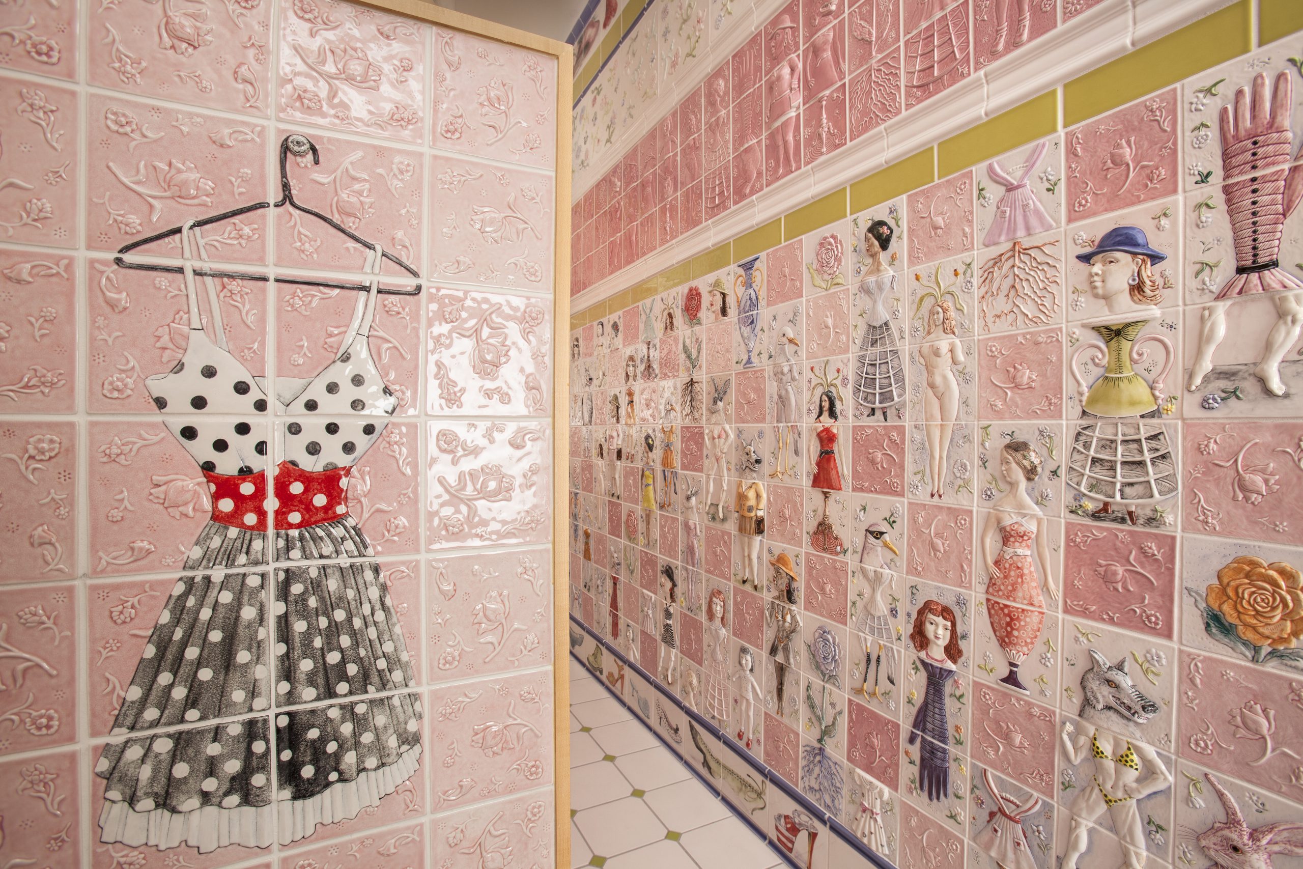 A detail of a pink bathroom with dresses and feminine forms on the tiles by Cynthia Consentino.