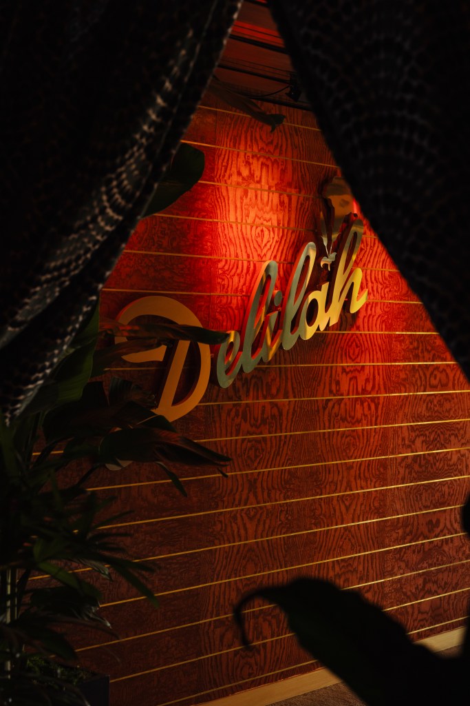 A wood panel wall lit in red with a large gold Delilah sign.