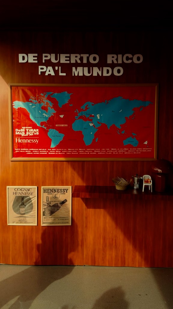 A red wall with a large red and blue map of the world with archival Hennessy photographs displayed under it.