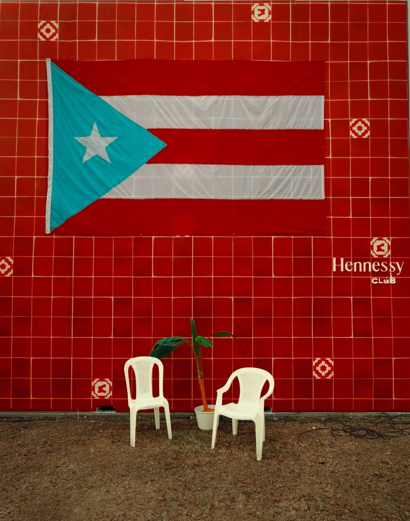 A large Puerto Rican flag hangs on a red tiled wall with two white plastic chairs sitting below it.